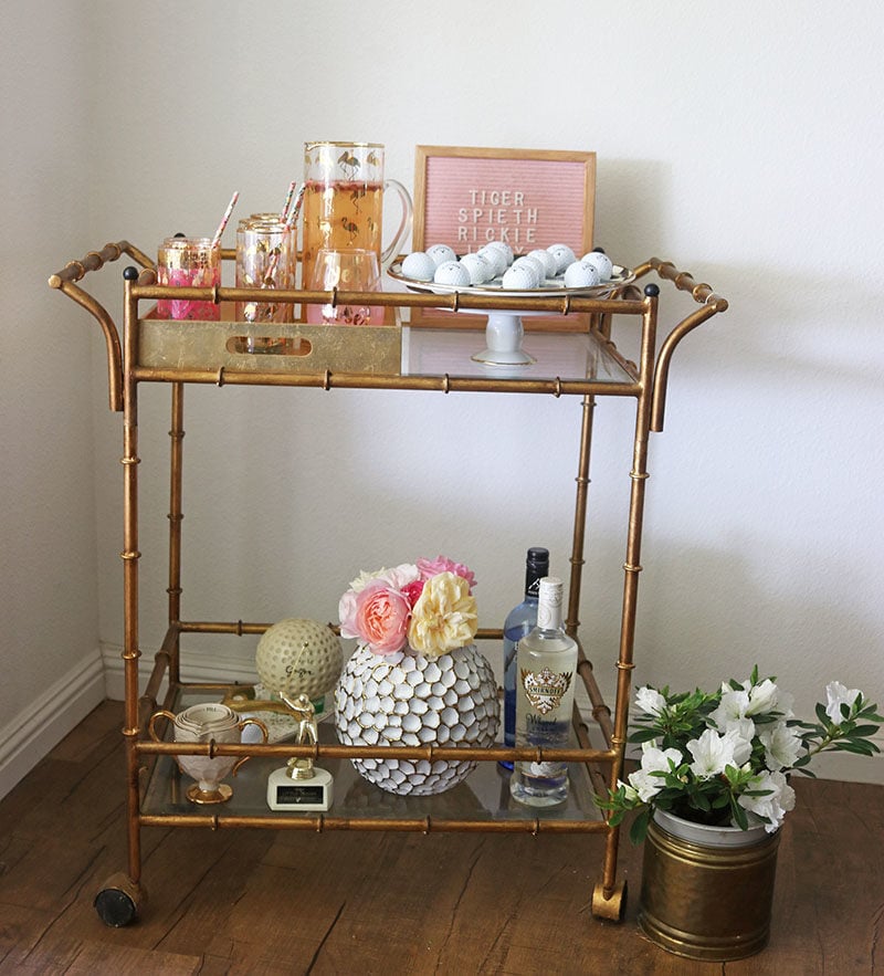 Blogger Candie Anderson shares her golf themed bar cart in gold filled with light pink decor, fresh flowers and golf balls.