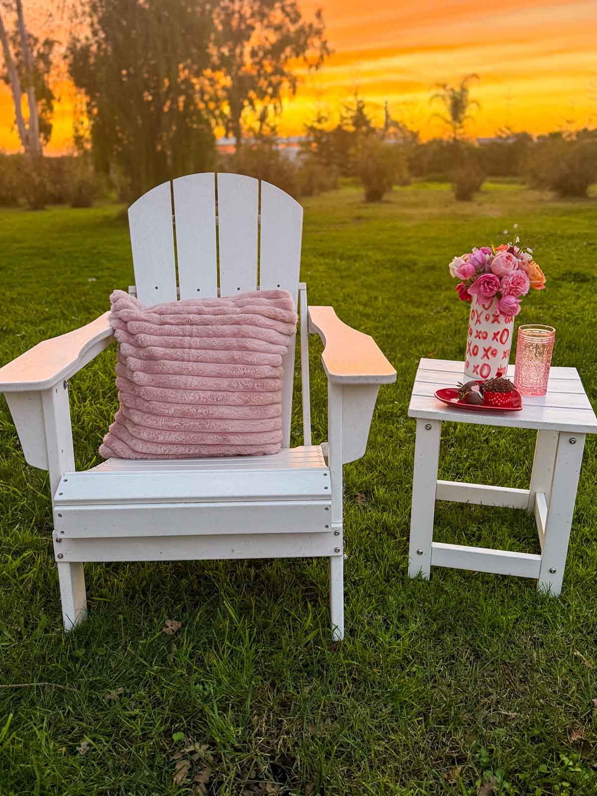 Entertaining expert, journalist and lifestyle blogger Candie Anderson of candieanderson.com shows how she adorned her white Adirondack chair with a cozy light pink faux fur throw pillow for Valentine's Day, and delicious desserts, beautiful flowers and a pink glass on her white outdoor side table.