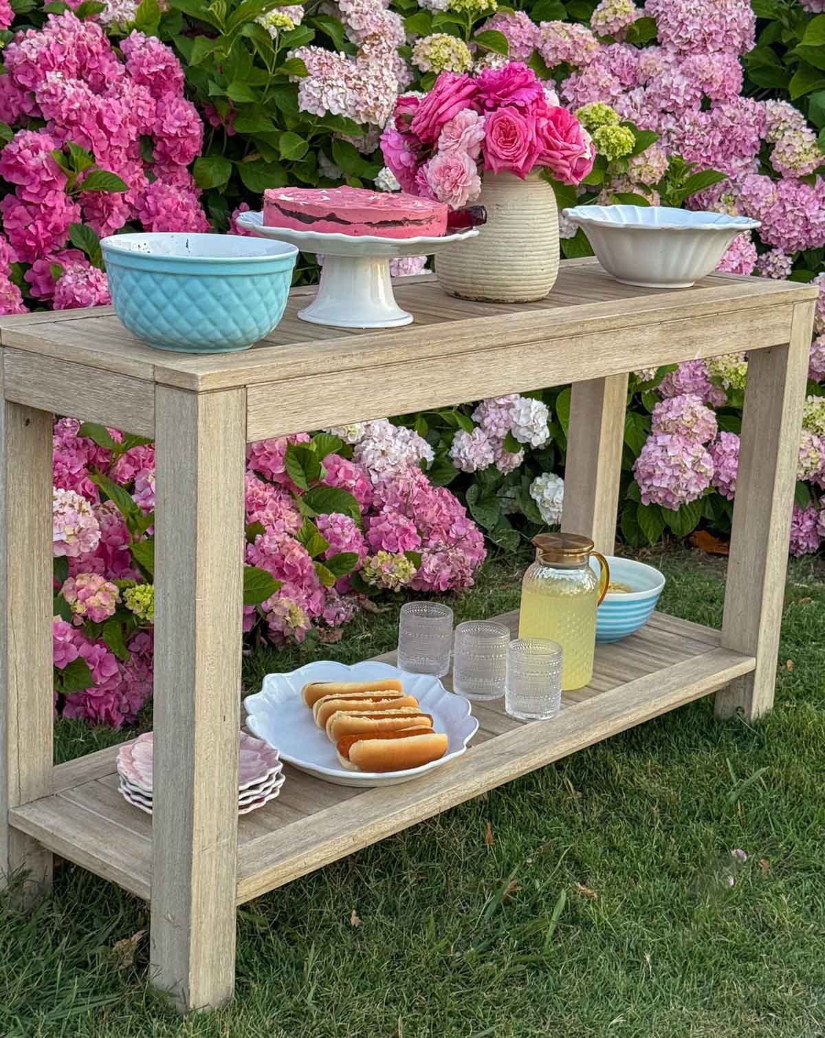 Entertaining expert, journalist and lifestyle blogger Candie Anderson of candieanderson.com shares her outdoor entertaining station with delicious pasta salad, corn salad, hot dogs, a homemade ice cream cake, chips, pink garden roses from her flower farm and her pink hydrangeas as the backdrop.