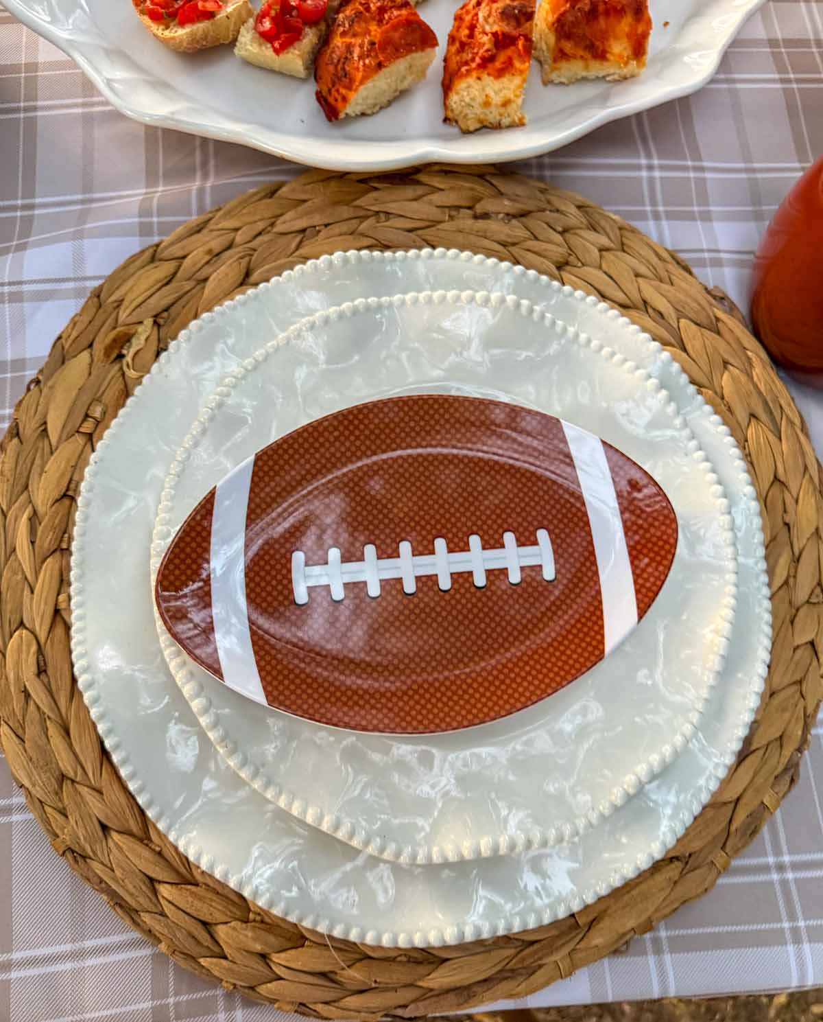 Entertaining expert, journalist and lifestyle blogger Candie Anderson of candieanderson.com shows you how to create the most perfect table setting for a football tailgate with a round woven charger, Perlette melamine dinner plates and salad plates and a football shaped plate on top.