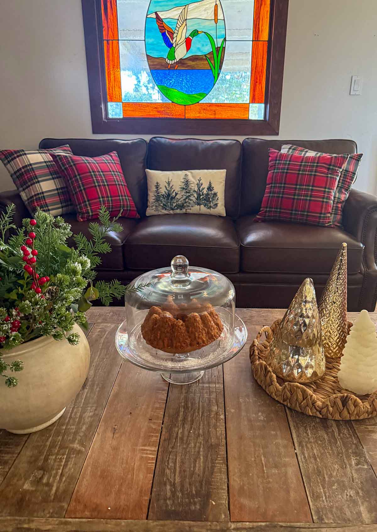 Lifestyle expert, journalist and interior design blogger Candie Anderson of candieanderson.com shares how she decorated her new Canora Grey leather sofa from Wayfair with beautiful plaid throw pillows and a winter throw pillow! She also decorated her rustic. coffee table with a forest cake in a glass cake stand and dome, metallic Christmas trees in a scalloped rattan tray, and fresh greenery and faux red berries in a ceramic vase.