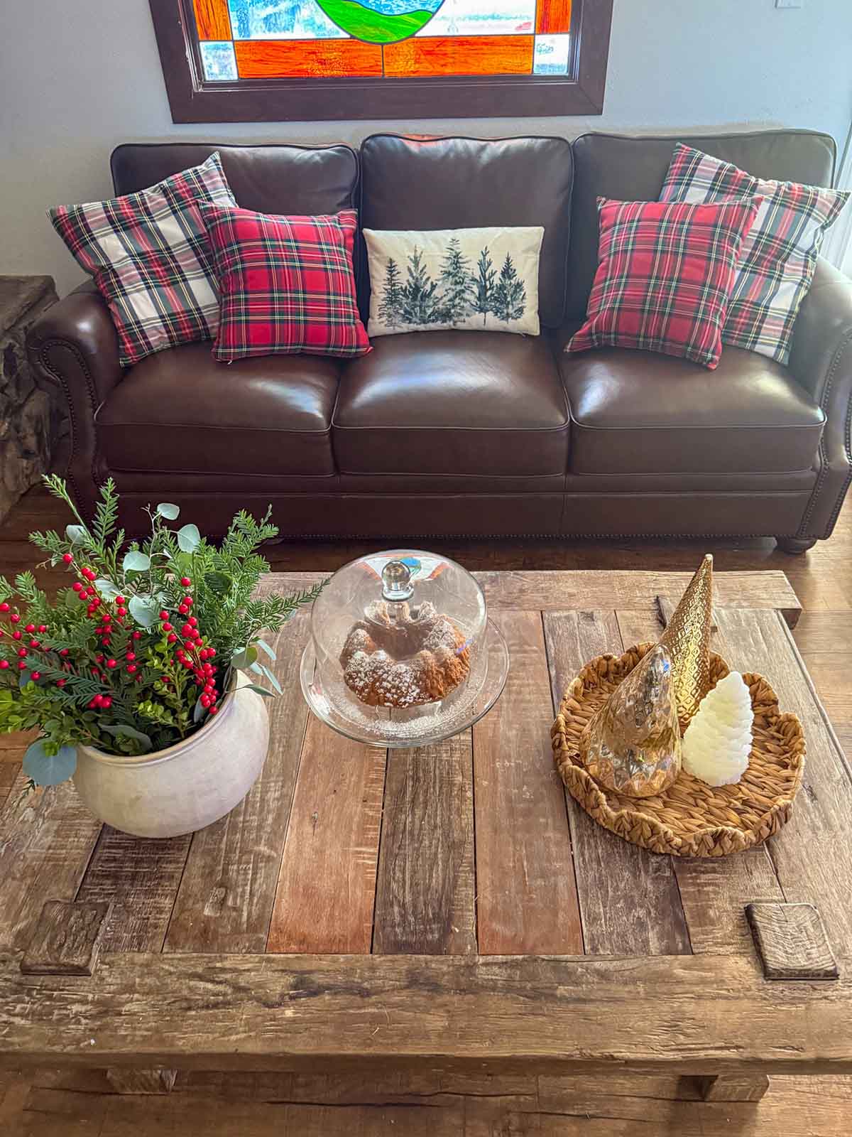 Lifestyle expert, journalist, and interior design blogger Candie Anderson of candieanderson.com shares how she decorated her Canora Grey Leather Sofa with classic Christmas plaid throw pillows and a winter throw pillow for the holidays. She also decorated her beautiful rustic coffee table with metallic Christmas trees, a scalloped rattan tray, a ceramic vase filled with fresh greenery and faux berries, and her delicious forest cake in a glass cake stand and dome.