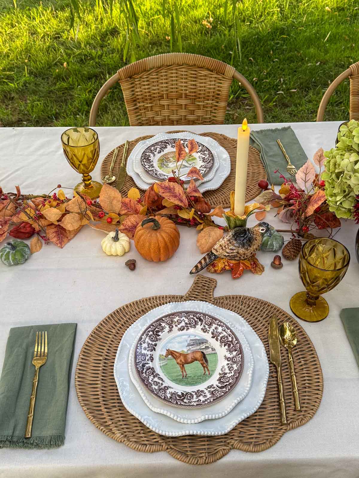 Entertaining expert, journalist and lifestyle blogger Candie Anderson of candieanderson.com shows how she created her elegant Thanksgiving tablescape with olive green fringe napkins, Spode equestrian horse plates, pumpkin shaped rattan placemats, amber goblets, a fall garland, a cream tablecloth and more.